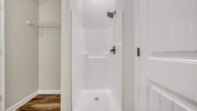 bathroom featuring wood finished floors, a shower stall, a walk in closet, and baseboards