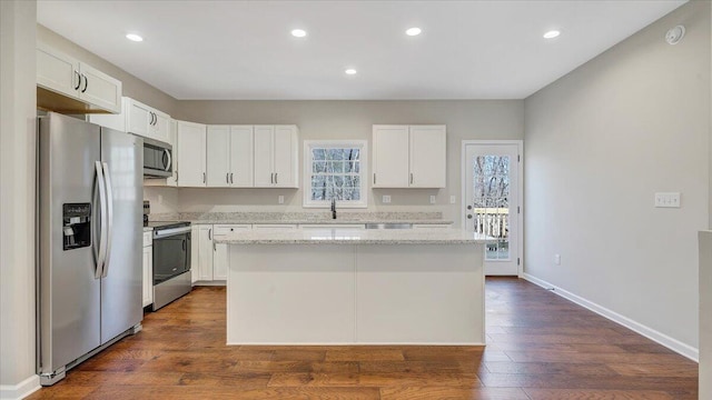 kitchen with stainless steel appliances, a center island, white cabinetry, and light stone countertops