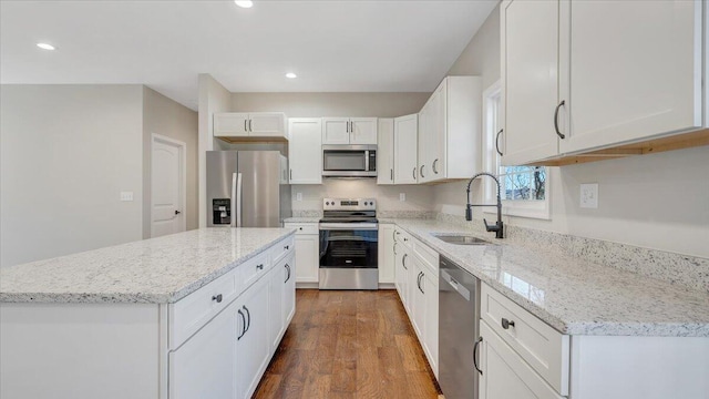 kitchen featuring light stone counters, stainless steel appliances, a sink, white cabinetry, and a center island