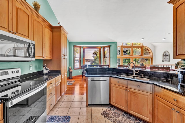 kitchen featuring stainless steel appliances, light hardwood / wood-style floors, dark stone counters, and sink