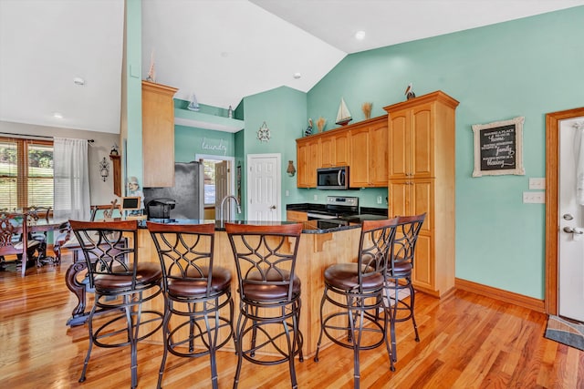 kitchen featuring appliances with stainless steel finishes, vaulted ceiling, kitchen peninsula, and light hardwood / wood-style flooring