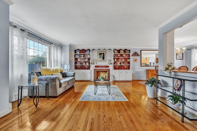 living room featuring light wood-type flooring, a fireplace, ornamental molding, and a notable chandelier