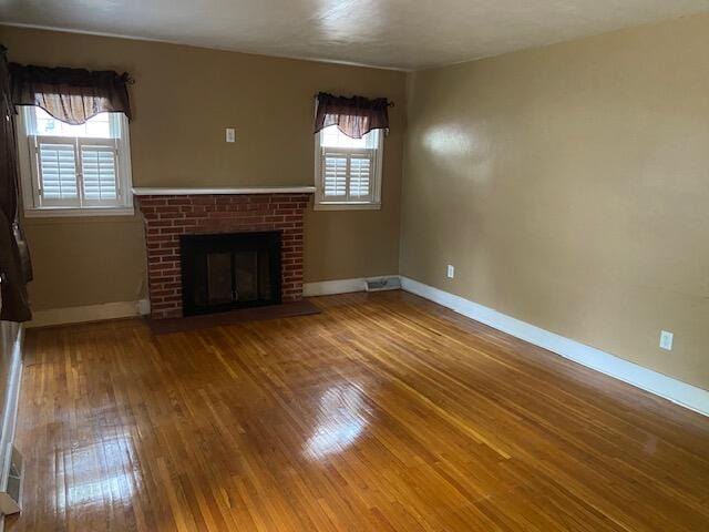 unfurnished living room featuring a healthy amount of sunlight, wood-type flooring, and a brick fireplace