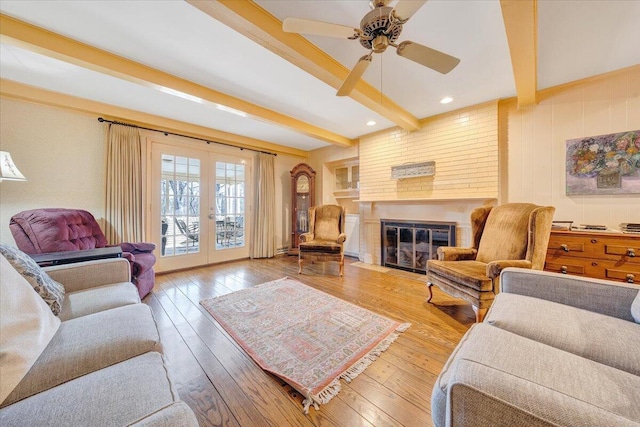 living room with french doors, a brick fireplace, ceiling fan, beam ceiling, and wood-type flooring