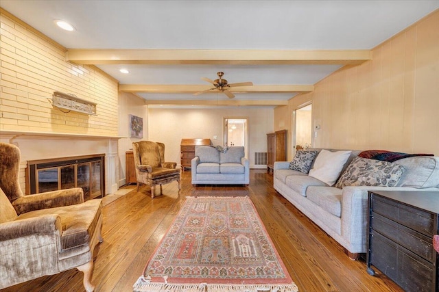 living room featuring hardwood / wood-style floors, ceiling fan, a fireplace, and beamed ceiling