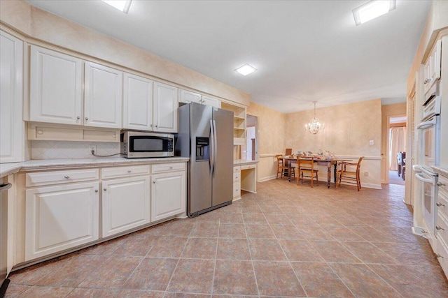 kitchen featuring pendant lighting, an inviting chandelier, tasteful backsplash, white cabinetry, and stainless steel appliances