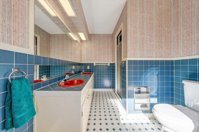 bathroom with walk in shower, vanity, tile walls, and toilet