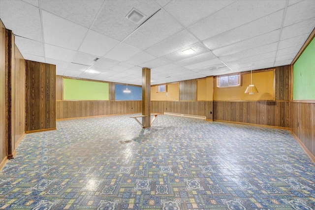 basement featuring a drop ceiling and wooden walls