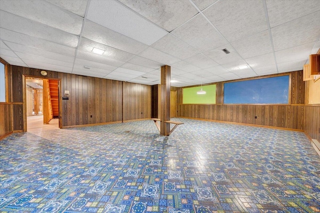 basement featuring a paneled ceiling and wooden walls