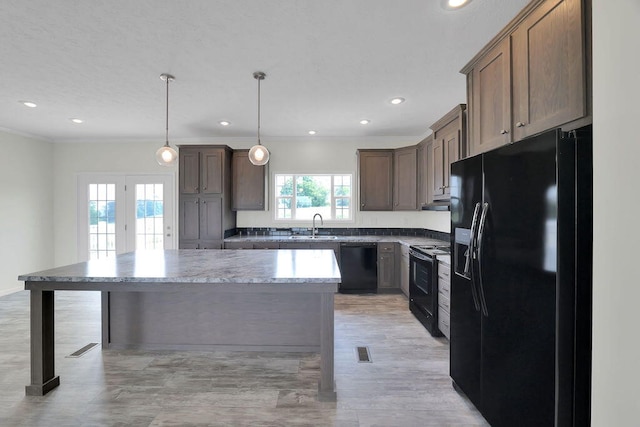 kitchen featuring a kitchen island, black appliances, pendant lighting, sink, and light stone counters