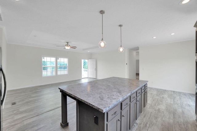 kitchen with light hardwood / wood-style flooring, a center island, ceiling fan, hanging light fixtures, and a raised ceiling