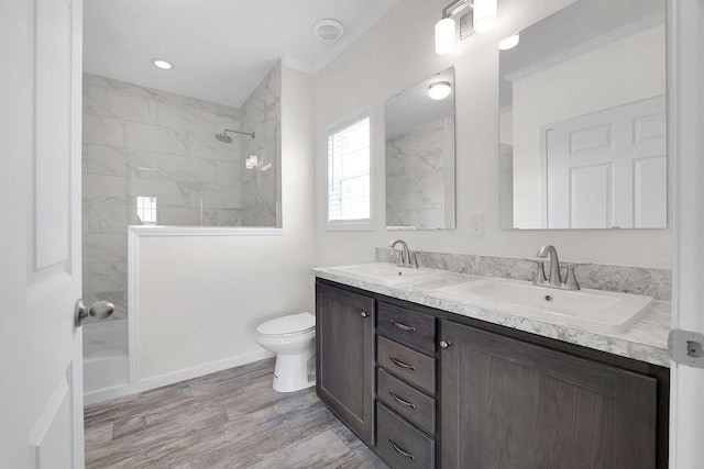 bathroom with hardwood / wood-style flooring, crown molding, toilet, tiled shower, and vanity