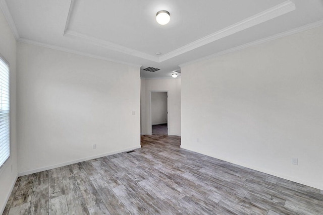 unfurnished room featuring crown molding, a raised ceiling, and light wood-type flooring