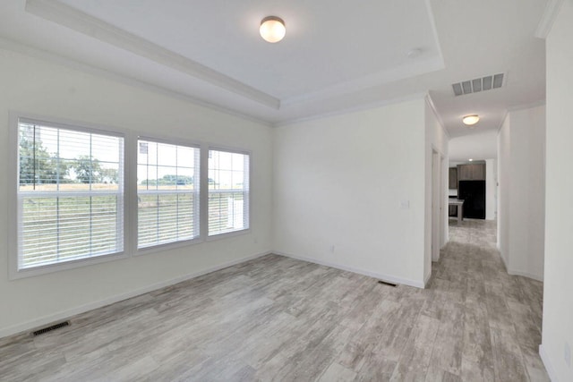 unfurnished room featuring a tray ceiling, light hardwood / wood-style floors, and ornamental molding