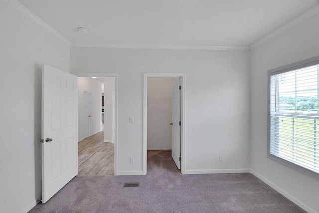 unfurnished bedroom featuring crown molding, light colored carpet, a spacious closet, and a closet