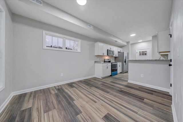 kitchen with white cabinets, appliances with stainless steel finishes, light stone counters, and dark wood-type flooring