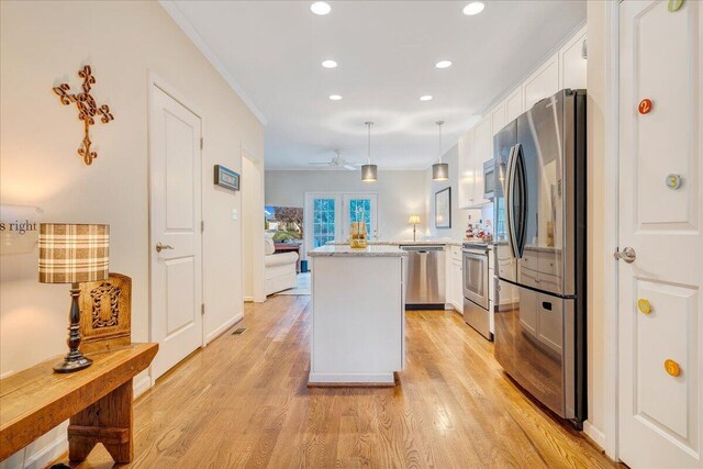 kitchen featuring light wood-type flooring, white cabinetry, hanging light fixtures, stainless steel appliances, and ornamental molding