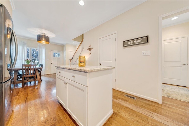 kitchen featuring ornamental molding, white cabinetry, stainless steel refrigerator, a center island, and light hardwood / wood-style floors