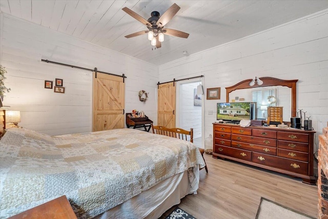 bedroom with ceiling fan, wooden walls, light hardwood / wood-style floors, wooden ceiling, and a barn door