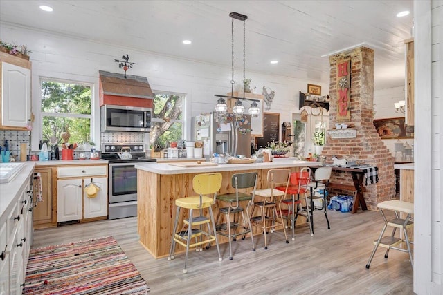 kitchen with a breakfast bar area, a kitchen island, pendant lighting, stainless steel appliances, and light hardwood / wood-style floors