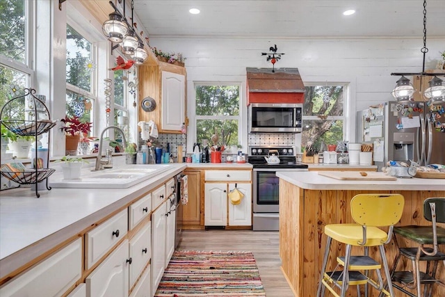 kitchen featuring a breakfast bar, sink, decorative light fixtures, light wood-type flooring, and stainless steel appliances