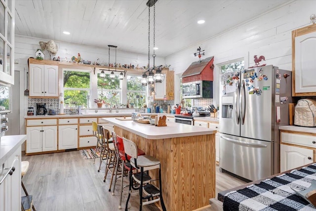 kitchen featuring a kitchen island, stainless steel appliances, tasteful backsplash, light hardwood / wood-style floors, and a kitchen bar