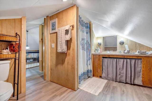 bathroom with vaulted ceiling, wood-type flooring, wooden walls, and toilet