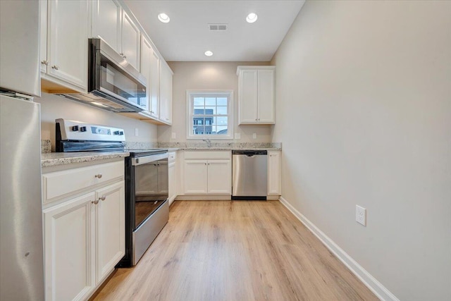 kitchen with white cabinets, light stone counters, stainless steel appliances, and light hardwood / wood-style flooring