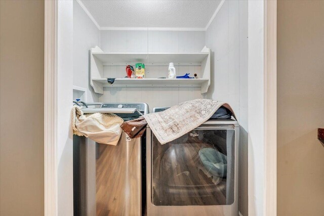 laundry room featuring a textured ceiling, washer and clothes dryer, crown molding, and wood walls