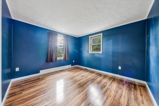 empty room featuring wood-type flooring, a textured ceiling, and crown molding