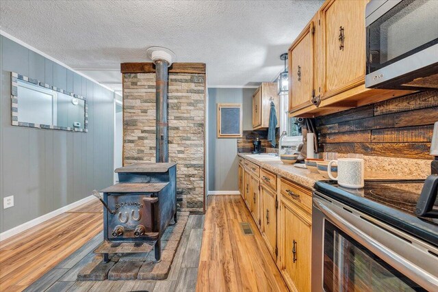 kitchen with a wood stove, stainless steel appliances, a textured ceiling, light hardwood / wood-style flooring, and sink