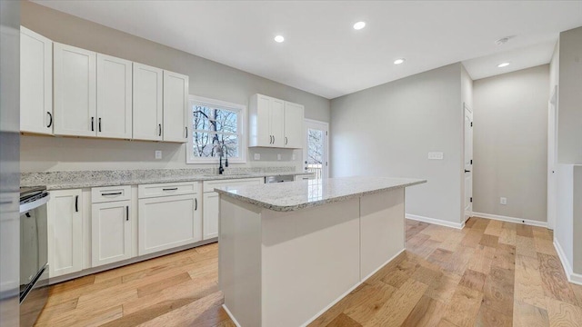 kitchen featuring a kitchen island, light stone counters, white cabinets, and a sink