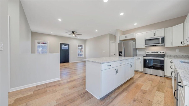 kitchen featuring stainless steel appliances, a kitchen island, white cabinetry, open floor plan, and light wood finished floors