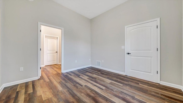 spare room with dark wood-style floors, visible vents, and baseboards