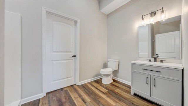 bathroom with toilet, baseboards, wood finished floors, and vanity