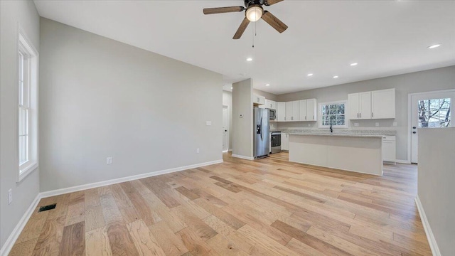 kitchen featuring light wood-style flooring, appliances with stainless steel finishes, white cabinetry, a kitchen island, and baseboards