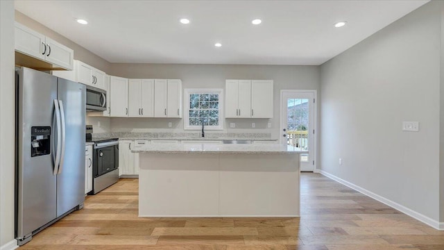 kitchen with light stone countertops, white cabinetry, a kitchen island, and appliances with stainless steel finishes