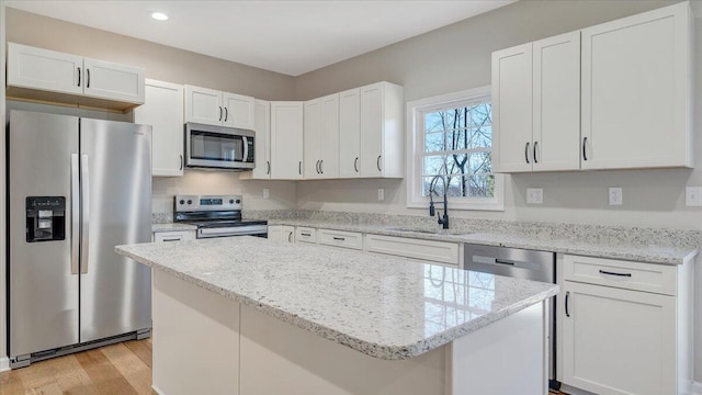 kitchen featuring white cabinets, appliances with stainless steel finishes, a center island, light wood-style floors, and a sink