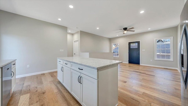 kitchen featuring light stone countertops, white cabinets, stainless steel dishwasher, and light wood finished floors