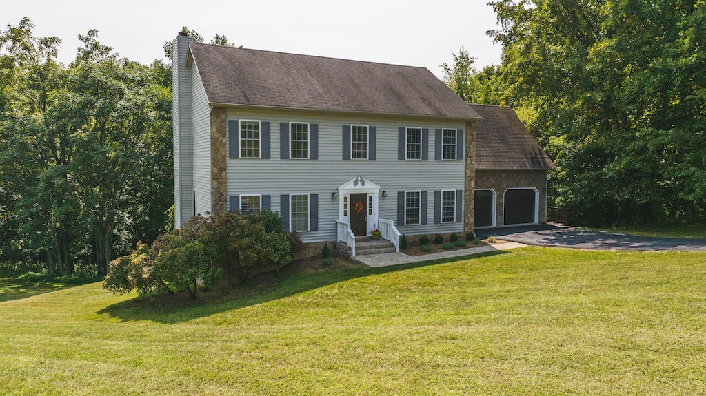 colonial inspired home featuring aphalt driveway, a front lawn, a chimney, and an attached garage