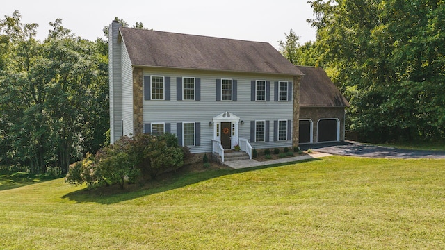 colonial inspired home featuring aphalt driveway, a front lawn, a chimney, and an attached garage