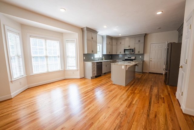 kitchen featuring gray cabinetry, light hardwood / wood-style flooring, a center island, appliances with stainless steel finishes, and a breakfast bar