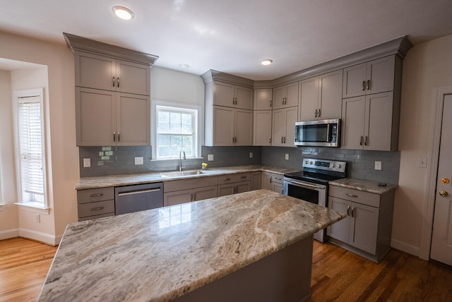 kitchen with light stone countertops, sink, stainless steel appliances, and hardwood / wood-style flooring