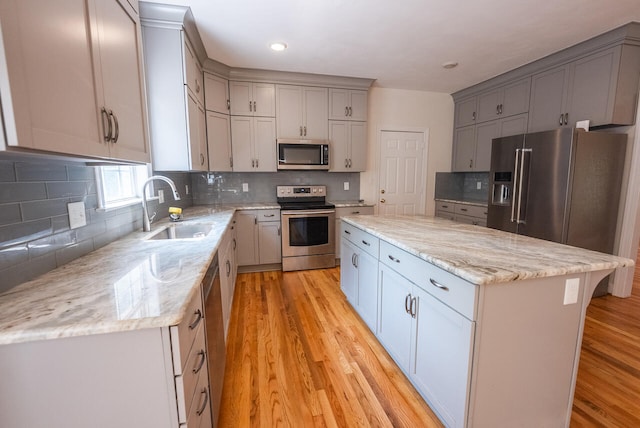 kitchen with light hardwood / wood-style floors, a kitchen island, light stone countertops, stainless steel appliances, and sink