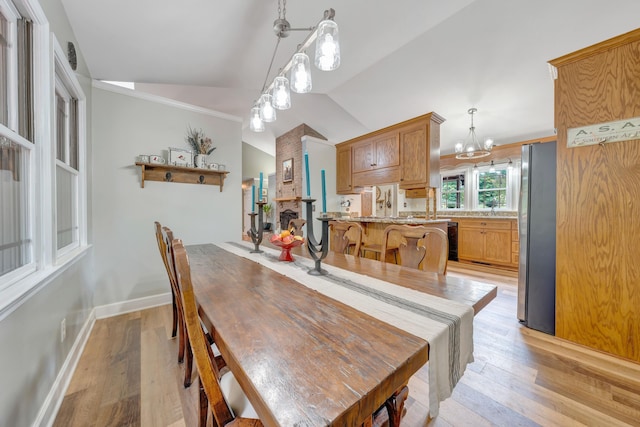 dining area featuring light wood-type flooring, crown molding, vaulted ceiling, and an inviting chandelier