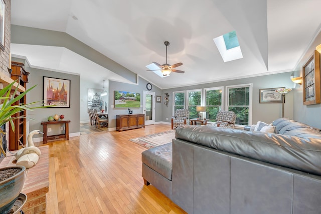 living room with ceiling fan, vaulted ceiling with skylight, and light hardwood / wood-style floors