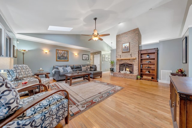 living room with a brick fireplace, light hardwood / wood-style floors, lofted ceiling with skylight, and ceiling fan