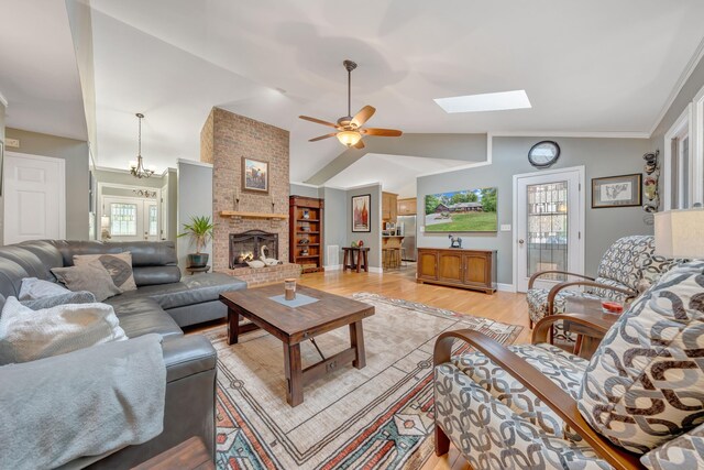 living room featuring vaulted ceiling with skylight, a fireplace, ceiling fan with notable chandelier, and light hardwood / wood-style flooring