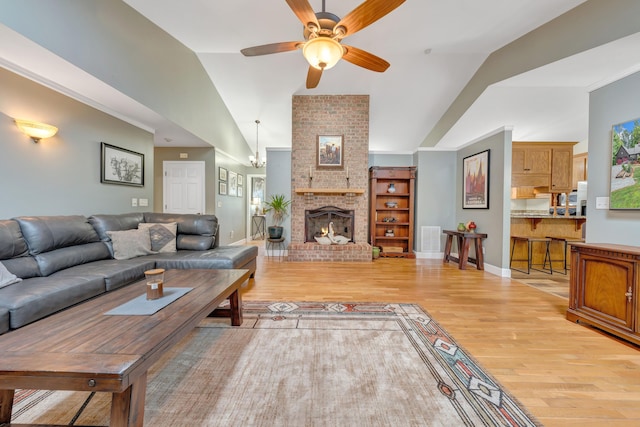 living room with a brick fireplace, lofted ceiling, ceiling fan, and light hardwood / wood-style flooring