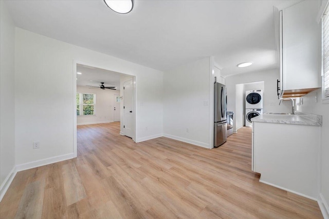 kitchen with white cabinets, stainless steel refrigerator, sink, light hardwood / wood-style floors, and stacked washer / dryer